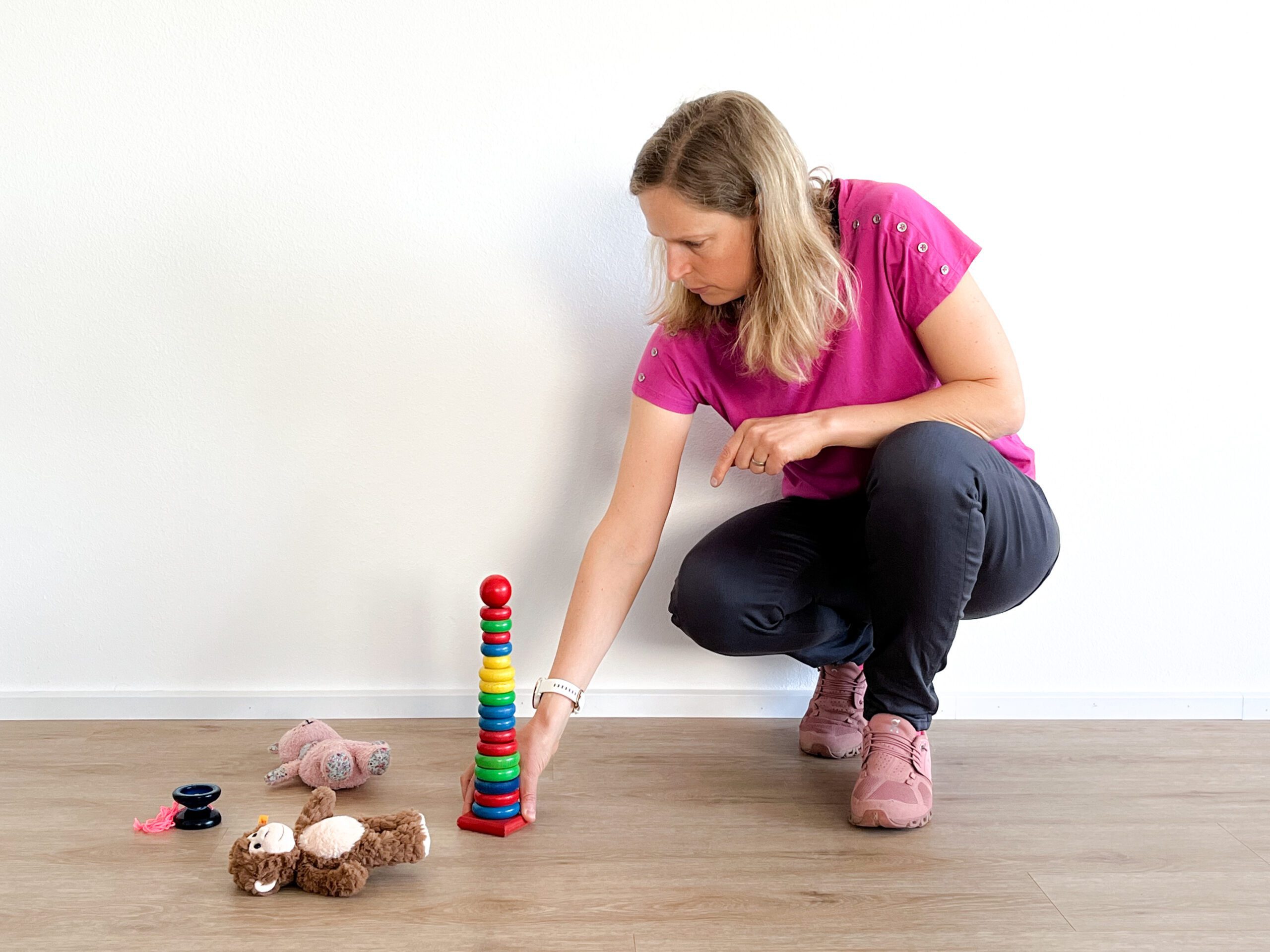 Frau spielt mit Kinderspielzeug am Boden.