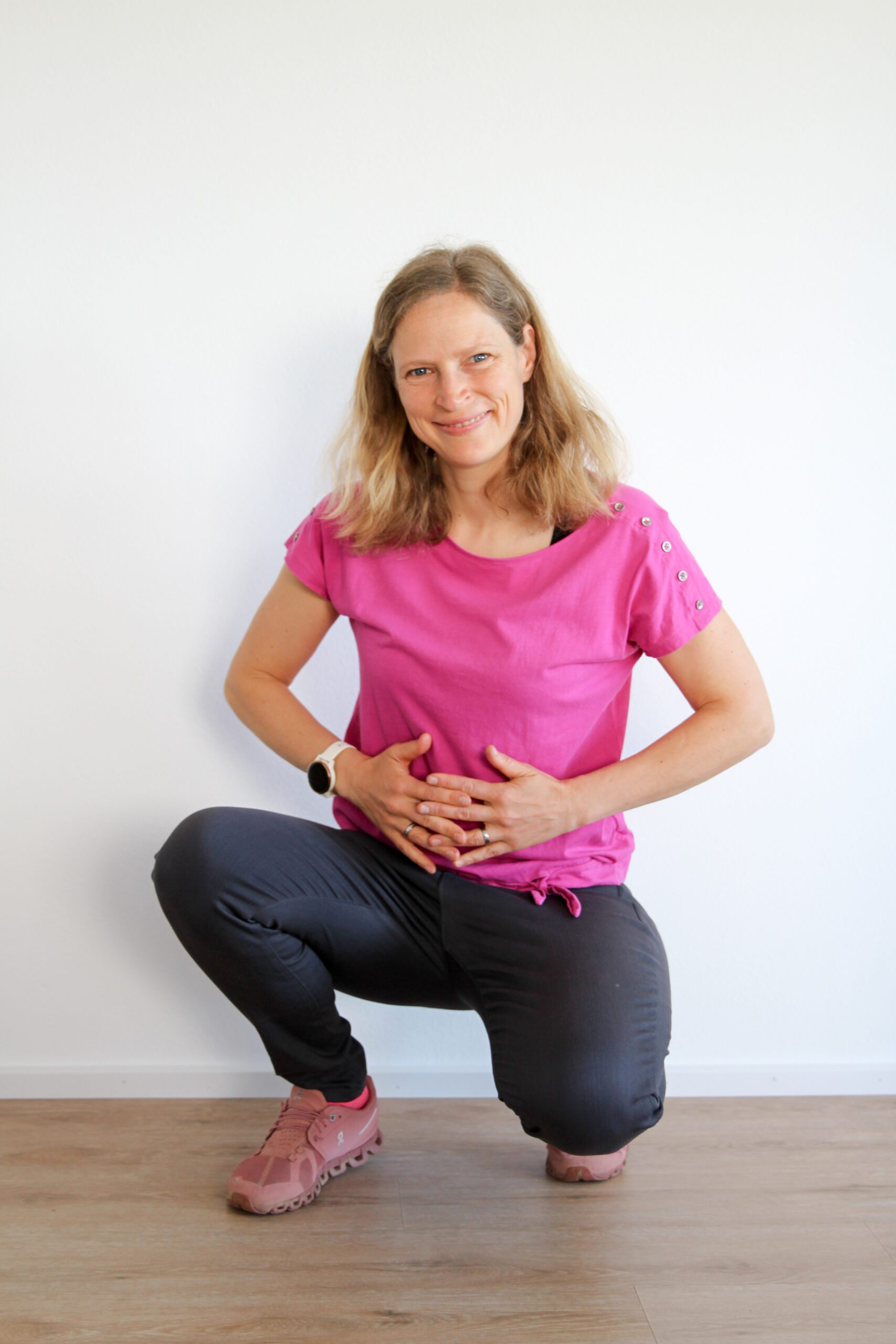 Frau in pinkem Shirt kniet lächelnd.