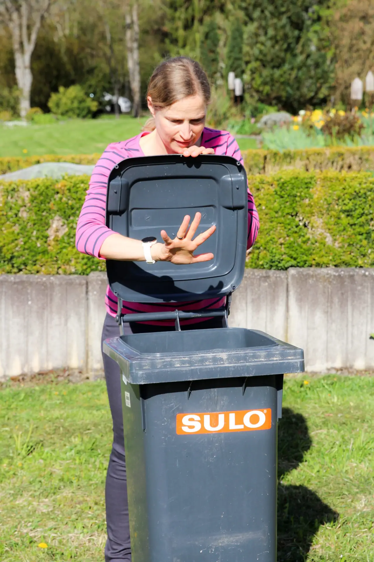 Frau lehnt sich über Mülltonne.