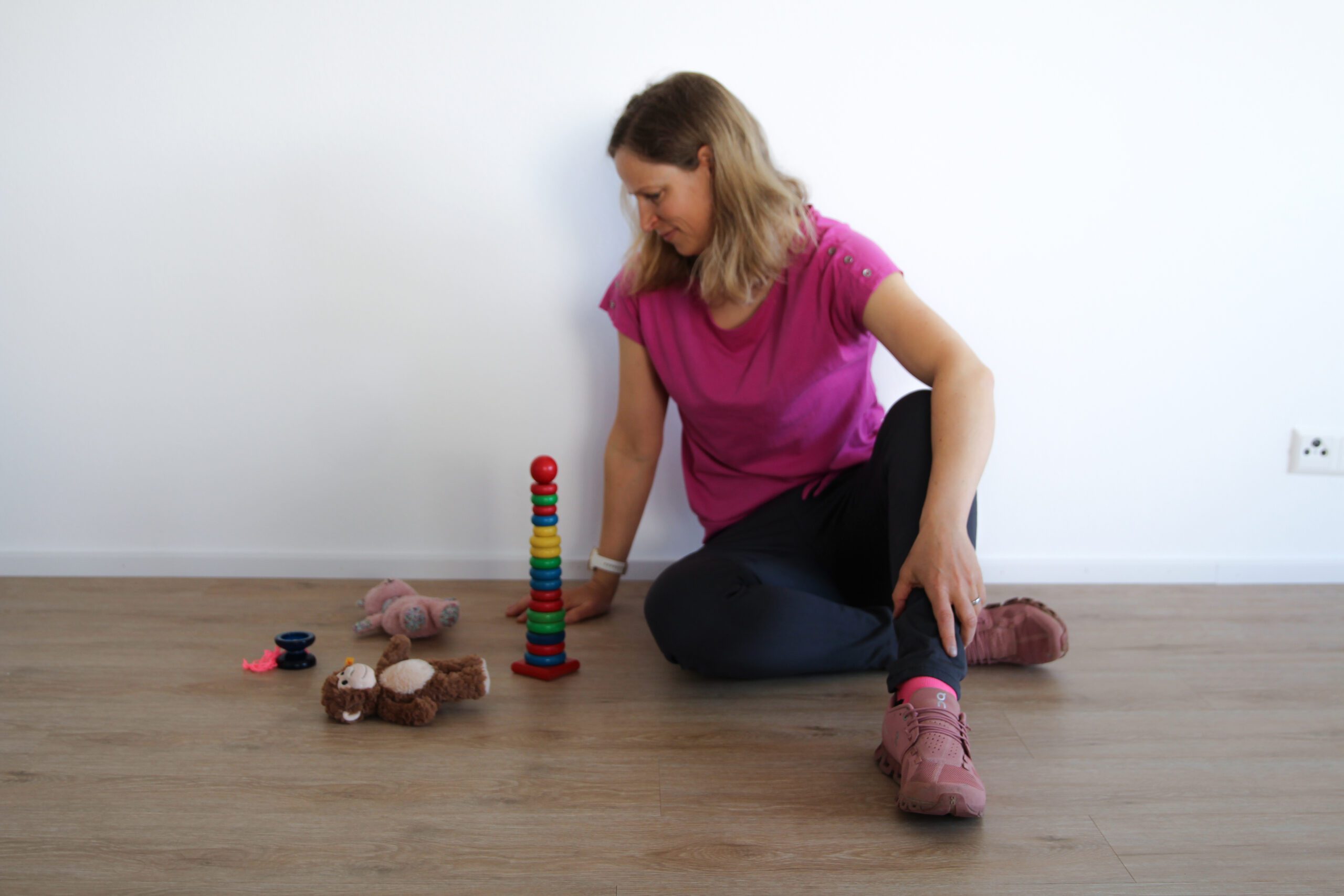 Frau spielt mit bunten Holzspielzeug auf Boden.